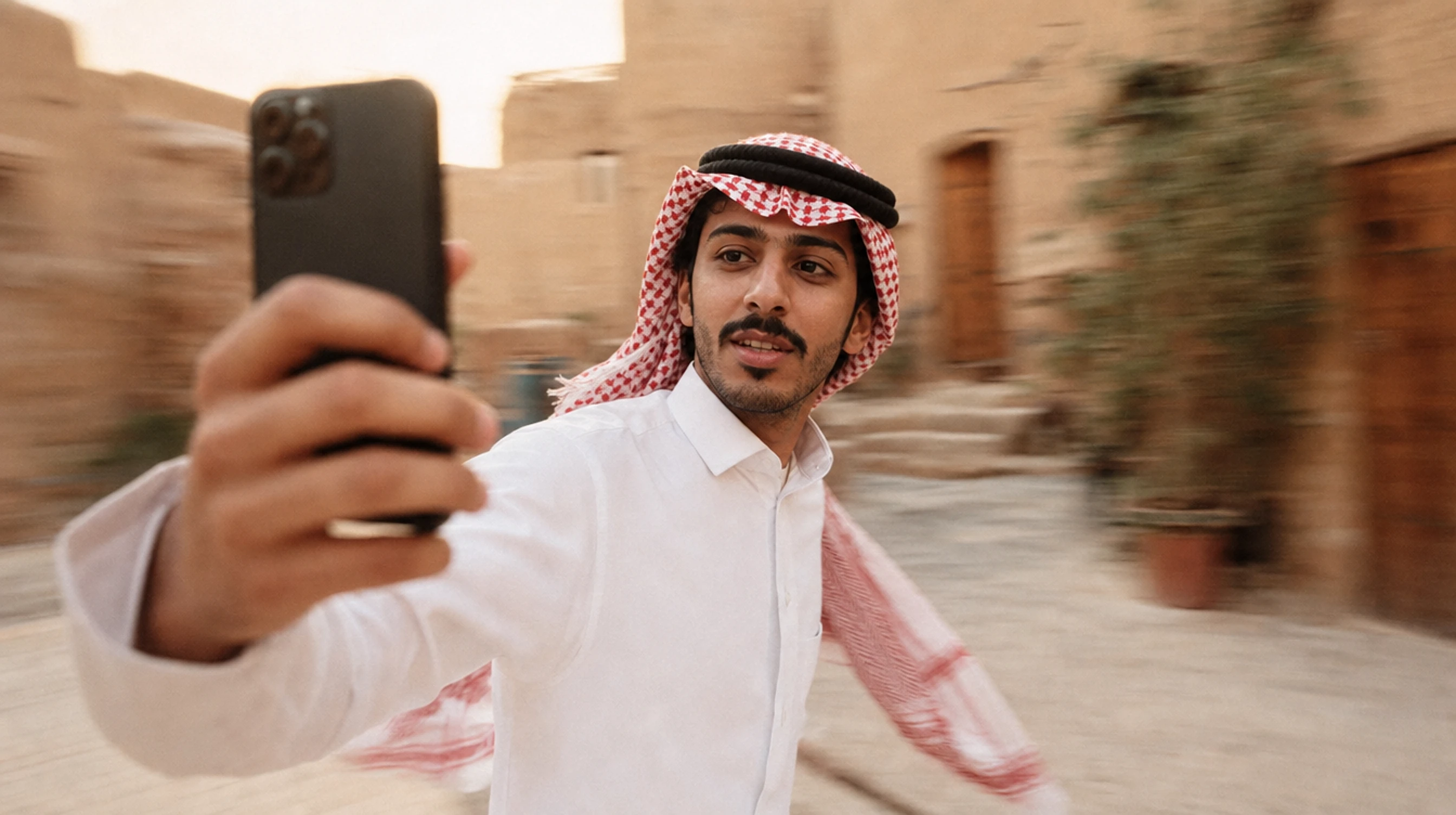 A Saudi content creator filming himself on his phone in a warm street