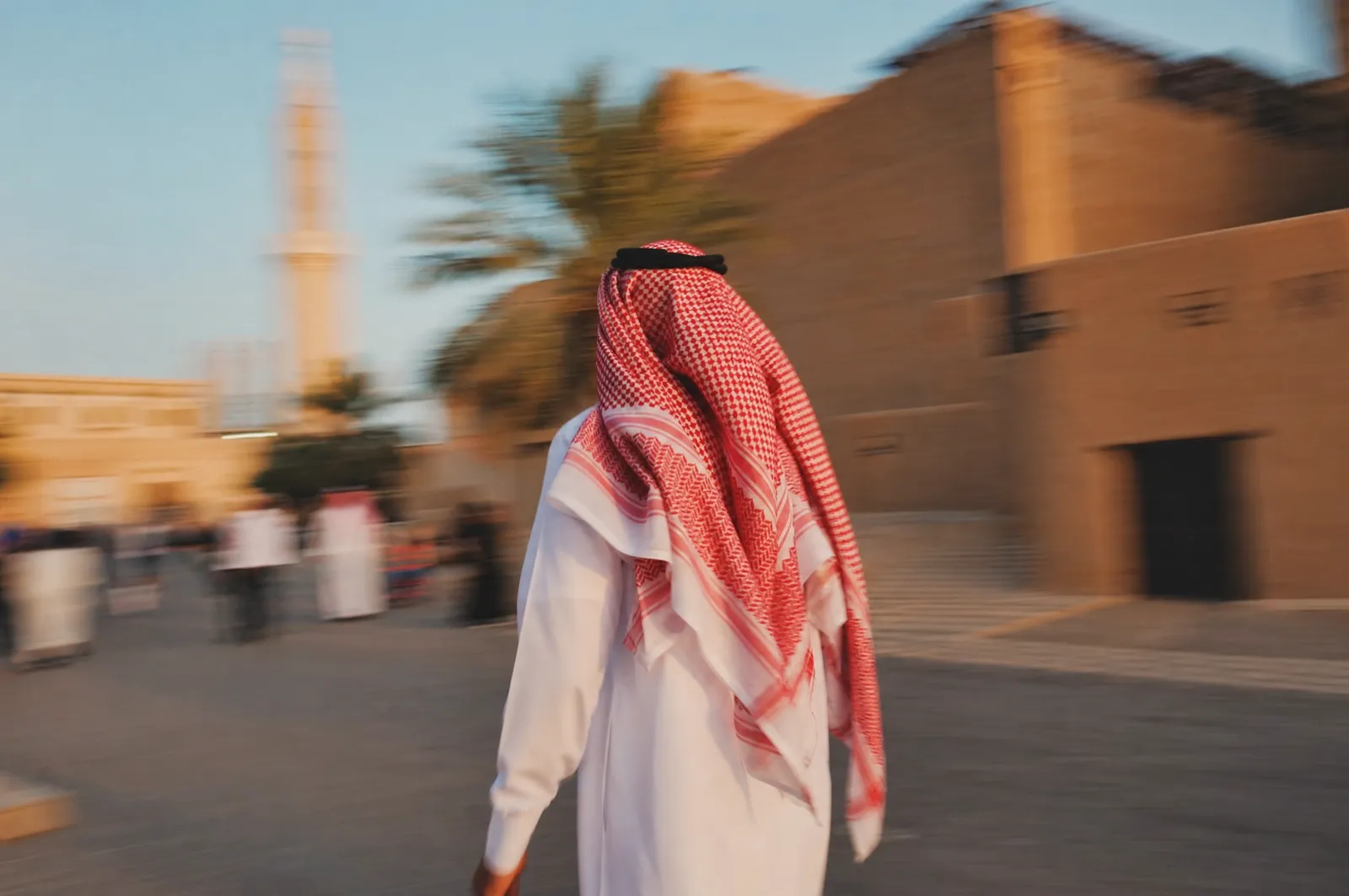 A Saudi man in thobe and shemagh walking fast, a warm photo with motion